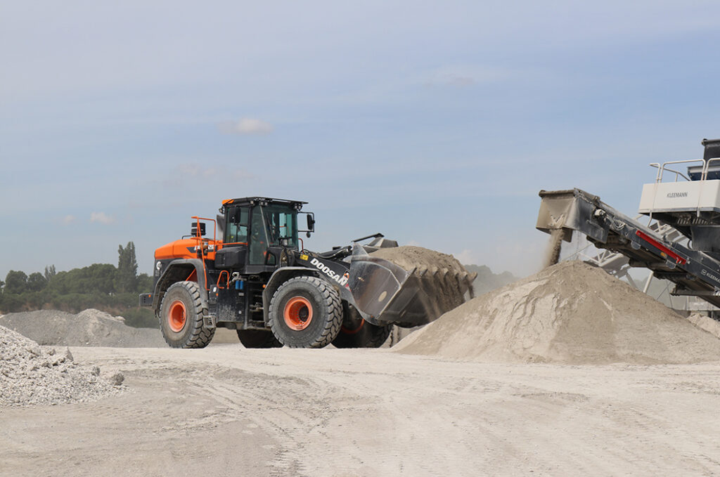 Ein großer oranger Schaufellader ist auf einer Baustelle aktiv, hebt eine Sandschaufel.